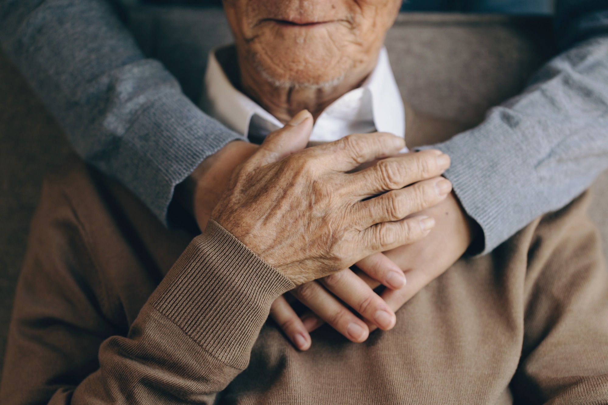 Happy healthcare worker hugging a senior man at home and support encouraging old people.