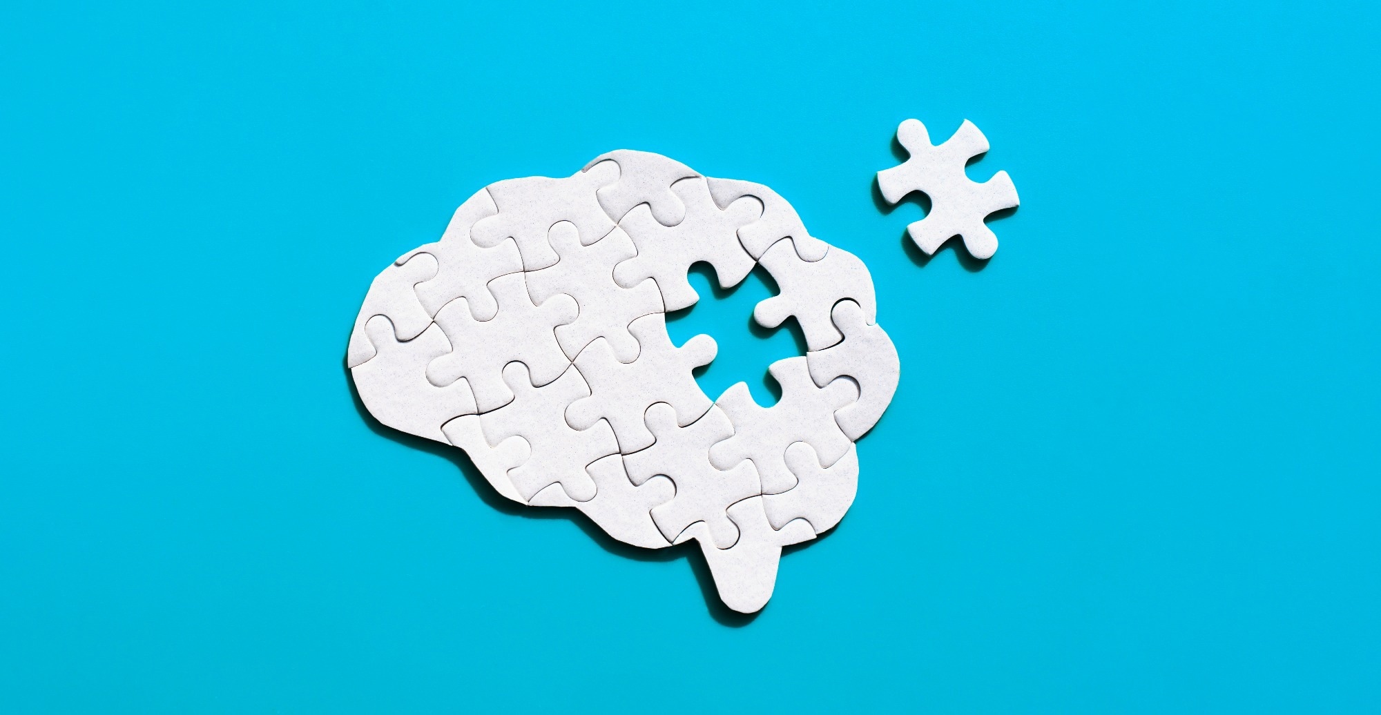 Picture of a human brain puzzle lacking a key element, against a serene blue backdrop.