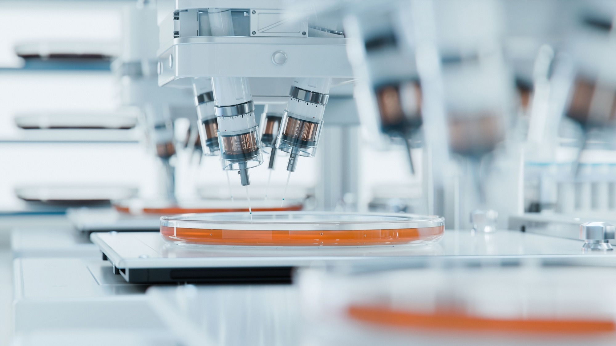 Robotic arms and pipettes work on petri dishes filled with an orange growth medium in a sterile laboratory