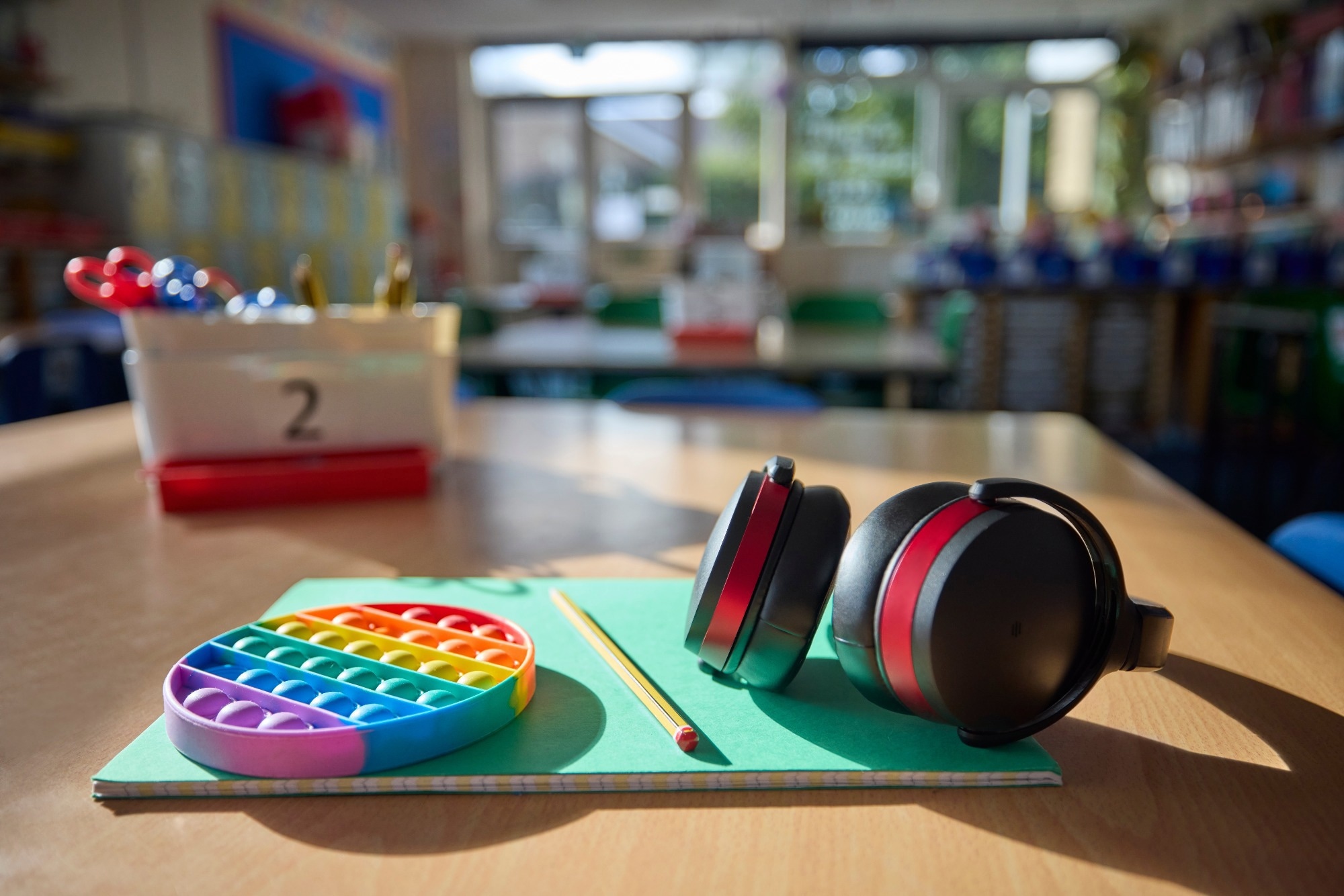 Ear Defenders Or Headphones And Fidget Toy To Help Child With ASD Or Autism On Table In School Classroom
