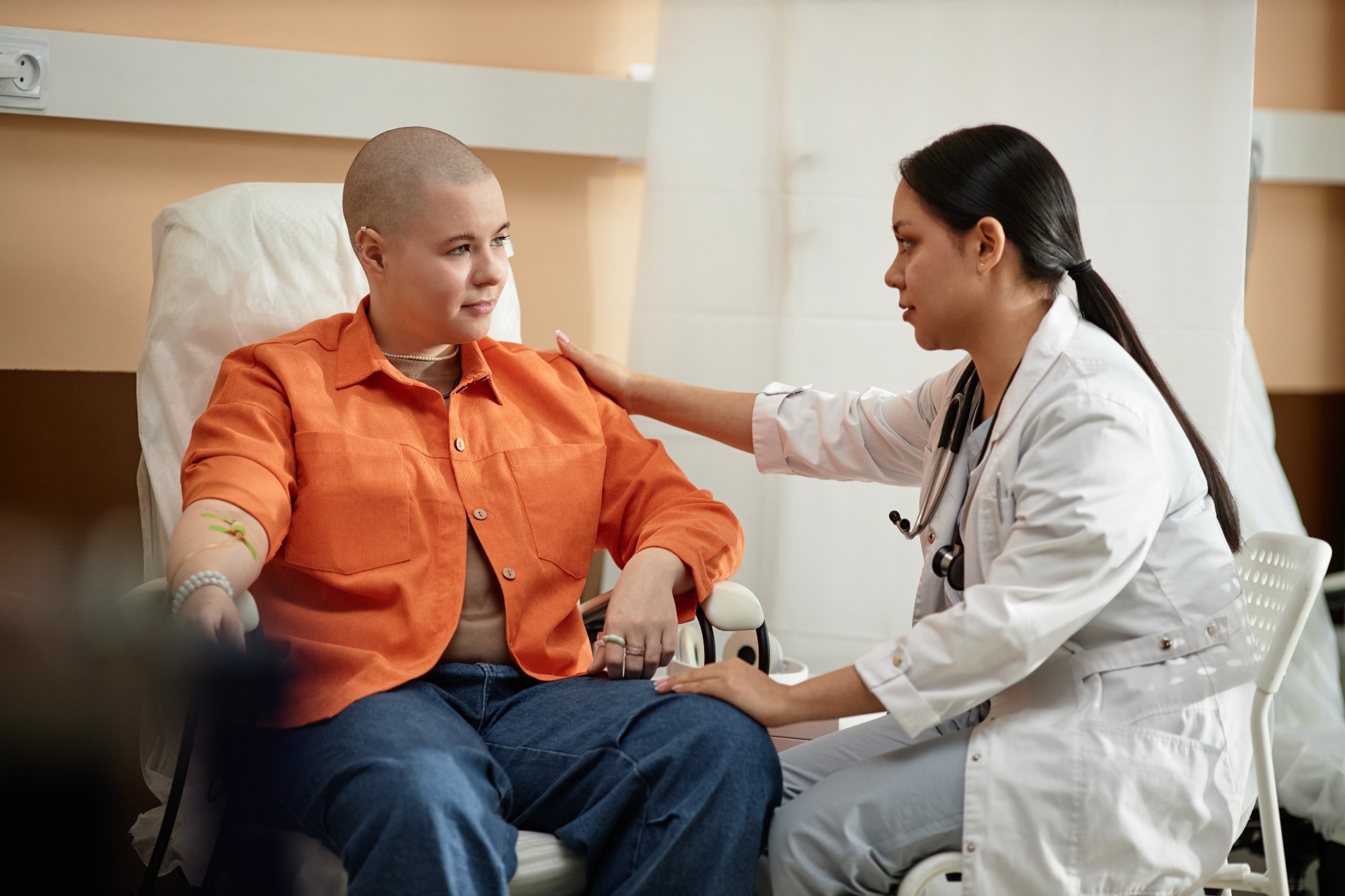 Side view portrait of young nurse comforting cancer patient receiving chemotherapy treatment in hospital