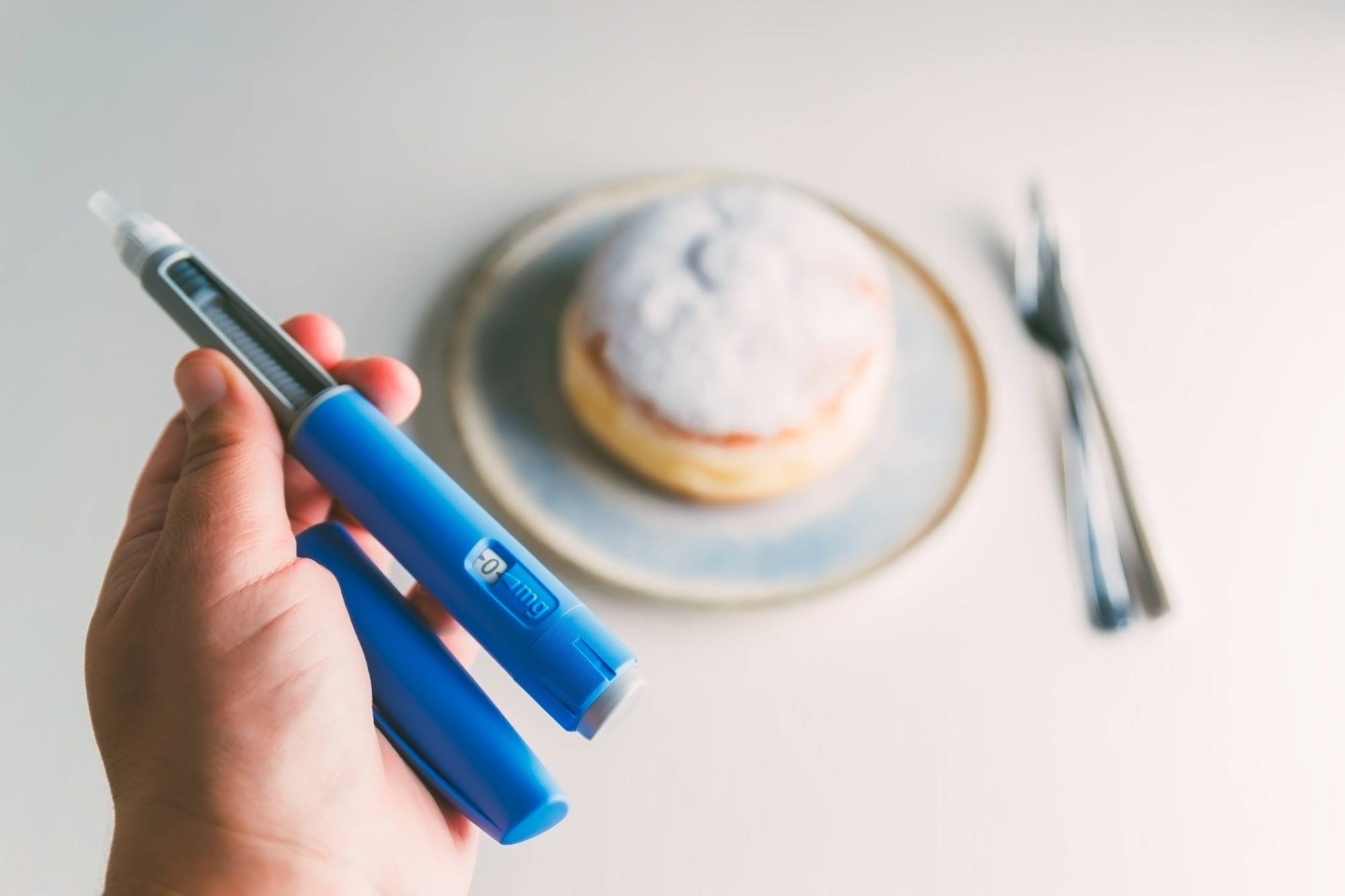Medical injection pen like ozempic for weight loss or diabetes treatment with a blurred sugary donut in the background.