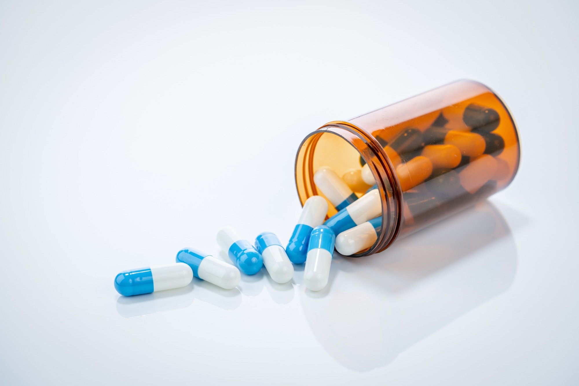 Prescription antibiotic capsules spilling from amber bottle on white background. Blue and white capsule pills.