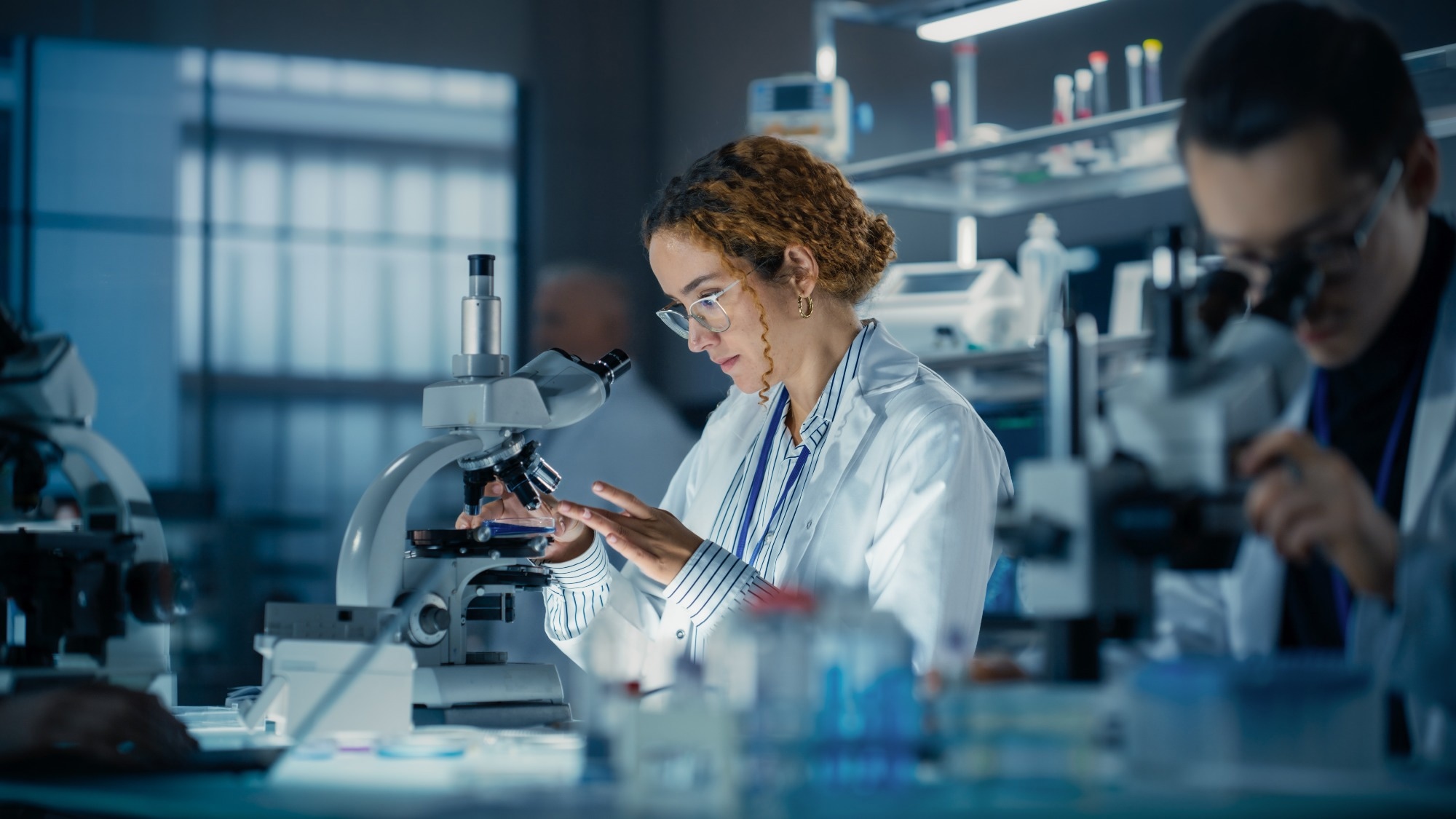 Hisplanic Female Bioengineer Looking at DNA Samples Under a Microscope in a Modern Applied Science Laboratory.